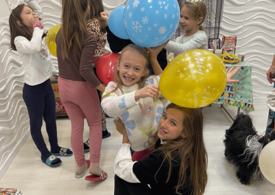 Gyerekek lufit tartva mosolyognak egy élményfestő születésnapi zsúron.